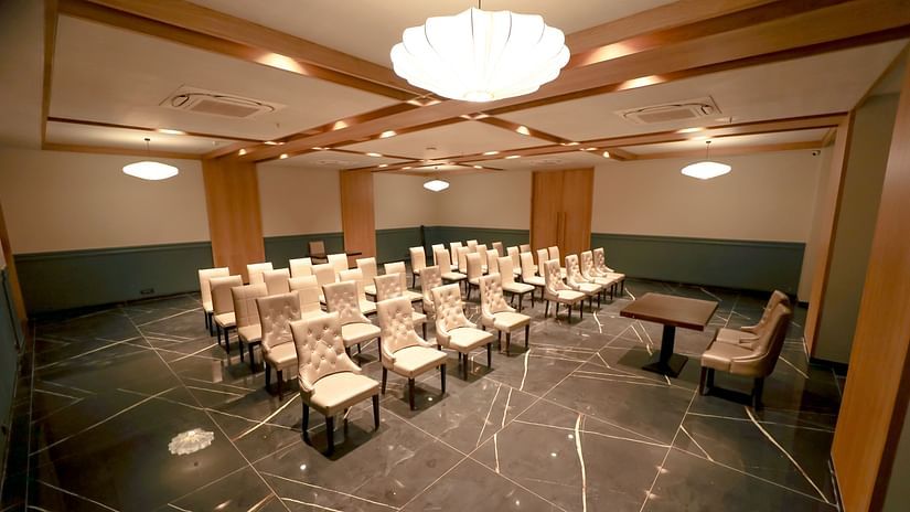 An image of a banquet hall with several chairs with a huge chandelier lights on top - Pride Resort Ambaji